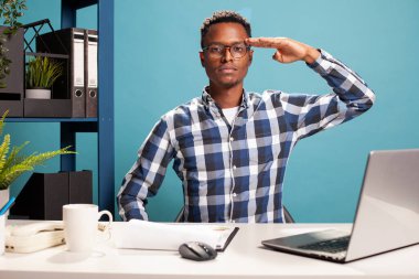 Afrika kökenli Amerikalı serbest çalışan masasında güven içinde oturuyor, eli alnında saygı ve vatanseverlik gösteriyor. Gözlüklü ciddi bir siyah adam, kameraya bakıyor ve selam veriyor..