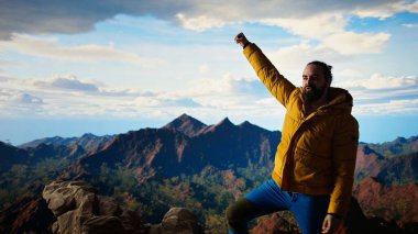 Açık hava kıyafetleri giymiş yürüyüşçü dağın zirvesine ulaşmasını kutluyor. Çarpıcı bir manzara ve tatmin duygusu macera ve kişisel gücün heyecanını temsil ediyor. Kamera A.