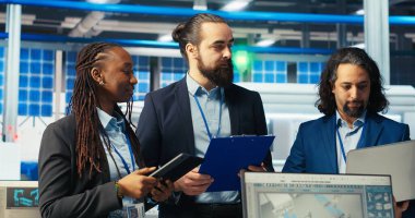 Fotovoltaik fabrikasında çalışan neşeli müfettişlerin arızalı sistem teşhisi koyan portresi. Mutlu yöneticilerden oluşan bir ekip güneş panellerini inceliyor fabrika üretimini azaltmak için, kamera B