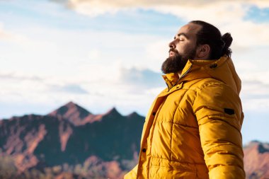 Genç maceracı dağın zirvesine ulaşıyor ve manzaraya hayran kalıyor, vadi manzarasını ve doğanın vahşi doğasını seviyor. Yürüyüşün ve gezinin tadını çıkaran bir yürüyüşçü..