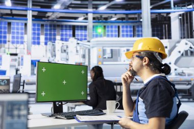 Fotovoltaik fabrikasında teknisyen güneş panelleri montaj süreçlerini geliştirmek için yeşil ekran bilgisayar kullanıyor. Mühendis, hassas güneş pilleri üretimi için ekipmanları kalibre etmek için bilgisayar kullanıyor.