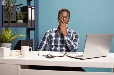 Eli çenesinde, şok olmuş bir ifadeyle, gözleri tamamen açık kameraya bakan Afrikalı Amerikalı bir menajer. Şaşırtıcı bir e-postayı okuduktan sonra ağzı açık kalan zenci bir işverenin portresi..