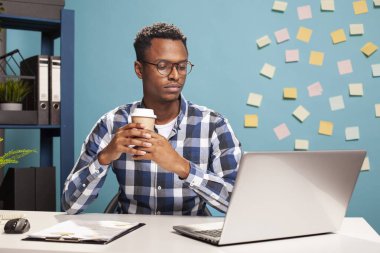 Uzaktan çalışan, çay içen ve bilgisayarında video kaydı olan kendine güvenen siyah bir adam. Profesyonel proje yöneticisi masada oturup kahveyi yudumluyor, sanal bir sınıfta..