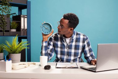 Şaşırmış bir erkek yönetici ofis masasında oturmuş ve saatine bakıyor. Toplantıya geç kalıyor. Gözlüklü Afrikalı Amerikalı iş adamı, saati kontrol ettikten sonra şok olmuş bir ifade takınıyor.