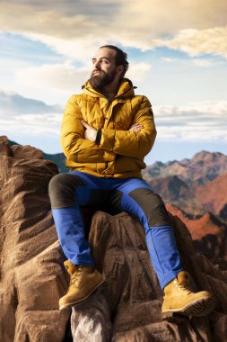 Bir dağ zirvesinde gezgin temiz havayı ve panoramik manzarayı içine çekiyor. Dağcı doğa aşığı engebeli tepelerin, engin gökyüzünün, maceranın ve gezinin çarpıcı manzarasına hayran kalır..