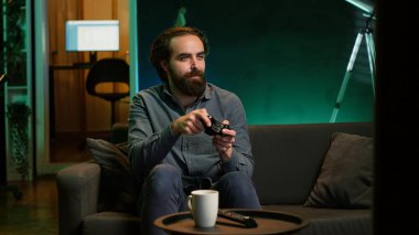 Neon ışıklı evde video oyunu oynayan mutlu bir adam, elinde kontrol cihazı tutuyor. Oyuncu çevrimiçi turnuvaya katılmak için heyecanlı, profesyonel joypad kullanarak diğer oyuncularla mücadele ediyor