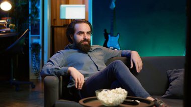 Komik komedi filmi izlerken koltukta oturup gülen, patlamış mısır yiyen eğlenceli bir adam. Apartman dairesinde atıştırmalık yiyen ve film sahnesinde komik bir şakayla eğlenen neşeli insan, kamera A