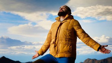 Gururlu kaşif, dağın zirvesinde kollarını kaldırıp, farkındalık içinde durarak başarının tadını çıkarıyor. Gezgin muhteşem manzaraya hayran ve yürüyüş heyecanı için uçsuz bucaksız gökyüzüne. Kamera B.