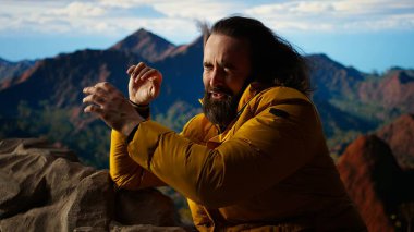 Erkek aktif gezgin, güzel dağ sırası vadisine hayran ama soğuk rüzgarlarla mücadele ediyor. Kamp alanındaki tehlikeli rüzgarlarla mücadele ediyor. Doğada gezinti tutkusu. Kamera A.