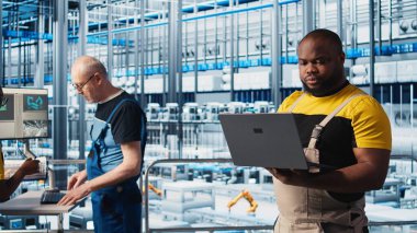 Sanayi 4.0 endüstriyel fabrika mühendisi robot makineleri yapay zeka teknolojisi kullanarak otomatikleştiriyor. Afro-Amerikalı adam akıllı fabrikada yapay zeka özelliklerini not defteri ve kamera A kullanarak uyguluyor.