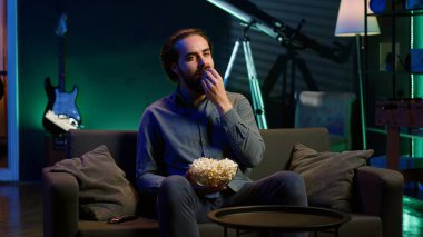 Uzaktan kumandayla televizyonu açan, evde boş vakitlerin tadını çıkaran, patlamış mısır yiyen bir adam. Aydınlatılmış apartman dairesinde, televizyon ve kamera A tarafından eğlendirilmiş, tuzlu atıştırmalıklar yiyen patates adam.