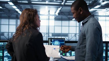 Veri merkezi ekibi sunucu odasındaki evrakları inceliyor, tabletteki yapay zekayı kullanarak sistem raporlarını analiz ediyor. Yapay zeka sunucu odası yöneticileri mali belgelere bakıyor, kamera B