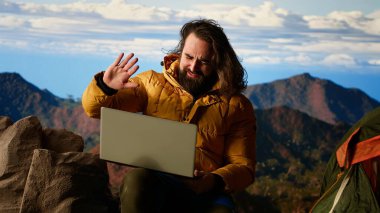 Dağ maceracısı, aşırı rüzgara rağmen dizüstü bilgisayarı üzerinde çalışarak çevrimiçi işini güvenlikten üstün tutuyor. Nefes kesen manzara, onun internet bağımlılığı tarafından gölgeleniyor. Kamera B.