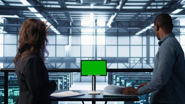 Mühendisler sunucu odasını model cihazıyla denetliyor, donanım belgelerini okuyor. Ekip sunucu merkezinde inceleme yapıyor, yeşil ekran tableti ve B kamerasıyla ilgili teknik dosyaları okuyor.