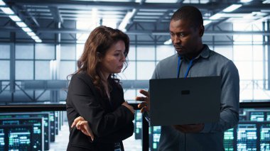 Veri merkezindeki geliştiriciler dizüstü bilgisayarda kodlama, ölçümleri analiz etme, depolama hacmini optimize etme. Bilgi işlem uzmanları sunucu odasında dizüstü bilgisayar kullanarak, sorunsuz işlemler ve kamera B ile çalışıyorlar.