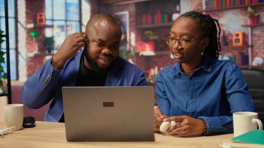 Afrika kökenli Amerikalı bir çift, internet yayını dinlemek için kulaklık kullanıyor ya da bir web platformunda online tartışmayı dinliyorlardı. Serbest çalışan erkek ve kadın masada vakit geçiriyorlar. Kamera A.