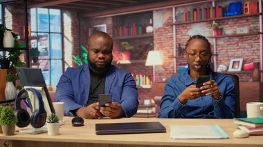 Oturma alanlarında yaşayan genç yetişkinler akıllı telefonlarıyla web sayfalarını karıştırırken masada oturup eğleniyorlar ve aletleriyle boş zamanlarının tadını çıkarıyorlar. Samimi bir daire. Kamera A.