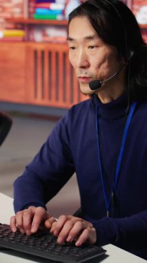 Dikey video, sevinçli teknik destek, çağrı merkezindeki üst düzey ajan sorun çözüyor. Jolly Tecrübeli Asyalı bilişim işçisi bilgisayar, kamera B kullanarak müşteri bağlantı sorunlarını düzeltiyor