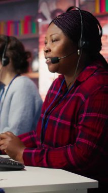 Dikey görüntüler gülen çağrı merkezi ajanı müşterilere dijital iletişim kanallarında yardımcı oluyor. Müşteri desteği çalışanı bilgisayarla müşteriyle canlı sohbet yapıyor, kamera B