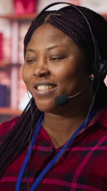Dikey video görüntüleme merkezi temsilcisi müşterilere rehberlik ediyor, soruları cevaplıyor. PC masasında çalışan neşeli Afrikalı Amerikalı müşteri merkezi çalışanı müşterileri teknik çözümler üzerinden yürütüyor.