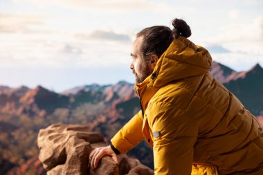 Erkek yürüyüşçü, tepenin zirvesinden nefes kesici bir dağ sırasına bakar ve büyük açık havanın yalnızlığını ve temiz havasını kucaklar. Macera hissi ve sonsuz doğa keşfi..