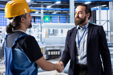 Fotovoltaik fabrikası müdürü ve mühendisi el sıkışıyor, sürdürülebilir yeşil enerji üretimi için anlaşmaya varıyorlar. Güneş panelleri tesisinde iş adamı el sıkışmayla ortaklığı tamamladı