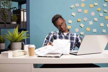 Mesaide yorgun düşmüş bir ofis çalışanı masasında oturmuş iş yoğunluğuyla boğuşan kağıtları fırlatıyor. Elinde belgeler tutan yorgun bir finans analistinin portresi. Üzüntüyle bakıyor..