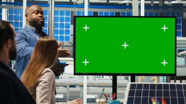 Fabrika hissedarları yeşil ekran monitörüne bakarak şirket büyümesinden bahsediyorlar. Yatırımcılar, üretimi geliştirmek için fabrika yöneticileriyle bir araya gelerek, sunuma ve B kamerasına bakıyorlar.
