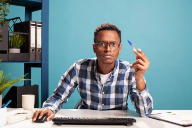 Şirket danışmanı elinde kalemle, bilgisayar ekranındaki iş harcamalarını yakından incelerken kafası karışık görünüyor. Siyahi girişimci, ofis masasında şüphe ve şüphe içinde oturmuş, verileri analiz ediyordu..