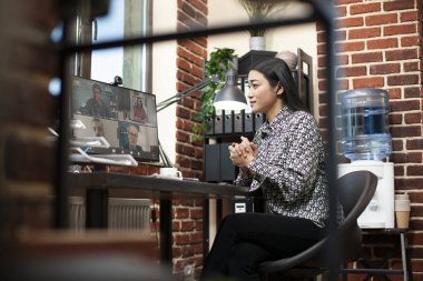 Profesyonel kadın masaüstü bilgisayarındaki online eğitim oturumunda takım üyeleriyle konuşuyor. Başlangıç ofisinde çalışan Asyalı bayan çalışanlar bilgisayardaki iş arkadaşlarıyla sanal toplantıya katılıyorlar.