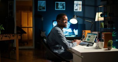 Evde cep telefonuyla kayan Afrikalı Amerikalı bir adamın portresi serbest görevlerine ve online işlerine ara veriyor. Sosyal medya uygulaması ve rahatlama üzerinden mesajlaşan genç yetişkinler. Kamera A.