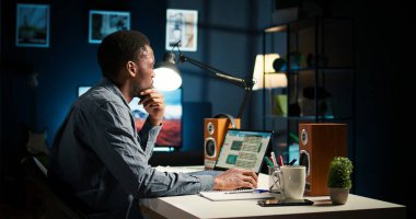 Serbest görevleri dengeleyen ve çevrimiçi verileri araştıran, makaleler için notlar ve bilgiler hazırlayan odaklanmış uzaktan çalışan. Siyahi biri evde çalışıyor, plan çizelgesi ve projeler yapıyor. Kamera A.