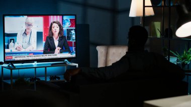 Geceleri, genç adam TV 'deki son manşetleri takip ediyor oturma odasındaki kanepede dinleniyor, haber programını izliyor. Uluslararası kanaldaki kişi yayınlanan bilgilere dikkat ediyor. Kamera B.