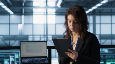 Yeni sunucu mimarileri yerleştirmek için tablet üzerinde yapay zeka teknolojisi kullanan veri merkezinde yönetici. Sunucu odasındaki kadın sabit performansı korumak için depolama sıralarını güncelliyor, kamera A
