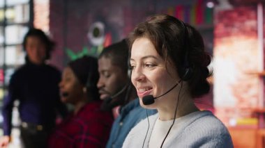 Ofisteki mutlu çağrı merkezi ajanı soruları cevaplayarak, sorunları çözerek müşterilere yardım ediyor. Müşteri hizmetlerindeki gülümseyen kadın bilgisayarın önünde müşterilerle konuşmak için kulaklık kullanıyor.