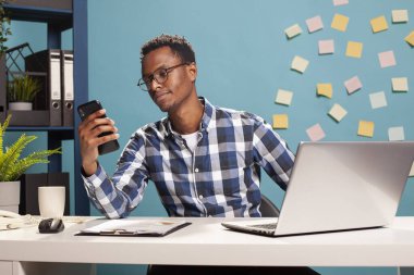 Genç serbest çalışan erkek masasında oturuyor ve cep telefonuna bakıyor. Akıllı telefonunu tutan Afrikalı Amerikalı danışman görevlerine ara verirken kısa mesajlar okuyor..