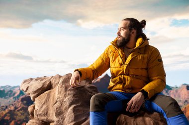 Yürüyüşçü, vahşi doğada yürümenin zorluğunu kucaklıyor, panoramik dağ manzarasının tadını çıkararak, gücün ve açık hava macerasının ödüllerini anımsatıyor. Macera Avcısı.