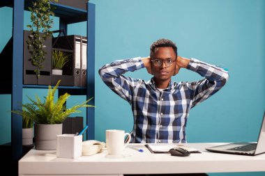 Afrikalı Amerikalı girişimci masasında oturmuş, kulaklarını kapatıyor ve kameraya bakıyordu. Kafasında elleri olan, ciddi bir ifadeye sahip siyahi bir serbest erkek portresi..