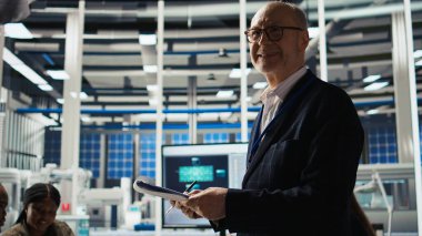 Güneş panellerindeki gülümseyen kıdemli mühendis verimliliği artırmak için bitki okuma belgeleri hazırlıyor. Fotovoltaik fabrikası araştırma ve geliştirme departmanındaki evrak dosyalarını kontrol eden yaşlı bir adam, kamera A