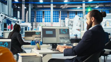 Robot kollarının performansını izlemek için PC kullanan Photovoltaics fabrika işçisi güneş panellerini montaj hatlarına yerleştiriyor. Bilgisayar masasında uzman, ekrana bakıyor, güneş santrali makinelerini inceliyor, kamera A
