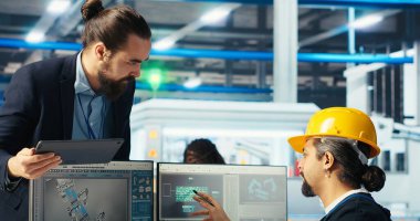 Fotovoltaik fabrikası mühendisi CAD yazılımında tesis katında çalışmayı planlıyor, takım liderini gösteriyor. Güneş panelleri üretim fabrikası teknisyeni montaj hatları tasarlıyor, bilgilendirme müdürü, kamera B