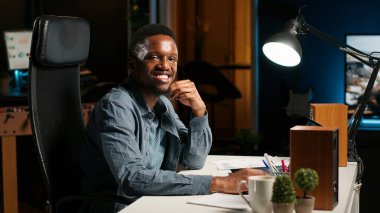 Serbest görevleri dengeleyen ve çevrimiçi verileri araştıran, makaleler için notlar ve bilgiler hazırlayan odaklanmış uzaktan çalışan. Siyahi biri evde çalışıyor, plan çizelgesi ve projeler yapıyor. Kamera B.