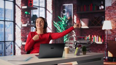 Kadın serbest çalışan, görevlerini etkili bir şekilde çözmek, evde çalışmak ve ses deneyimiyle birden fazla iş yapmak için kulaklıktaki ambiyans müziğini kullanıyor. Olgun bir kadın uzaktan işten zevk alıyor. Kamera B.