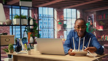 Evdeki siyahi kadın modemi ve sorun çözme rehberini inceliyor, kablosuz ağ yönlendiricisini tamir etmeye çalışıyor ve uzak bağımsız işler için internet bağlantısını onarmaya çalışıyor. Sinyal kaybı. Kamera A.