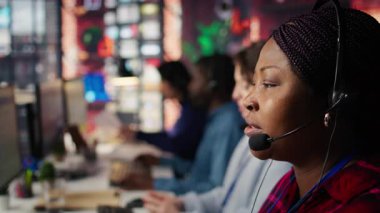 Çağrı merkezi çalışanı mikrofonla konuşur, müşteri soruşturmaları ve şikayetlerle ilgilenir. Afrika kökenli Amerikalı müşteri hizmetleri temsilcisi müşterilere sorunlarda yardımcı oluyor. Kamera B, kapat.