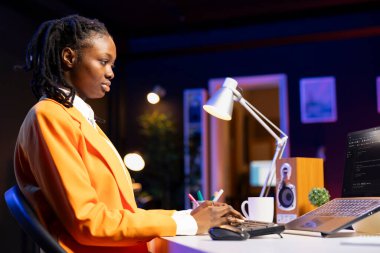 Sistem yöneticisi, daire ofisinde programlama dilleri kullanarak dizüstü bilgisayara kod yazar. Loş aydınlatılmış oturma odasından çalışırken genç bilişim uzmanı veritabanı hatalarını düzeltiyor