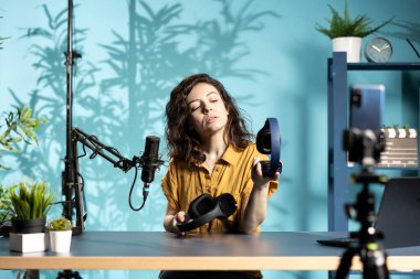 Edebiyat stüdyosundaki içerik yaratıcısı çevrimiçi yayın platformları için kablosuz kulaklık incelemesi çekiyor. Medya yıldızı internet şovu sunuyor, dinleyiciler için müzik dinleme aygıtı açıyor