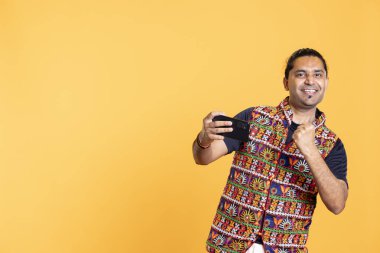 Akıllı telefondan maçı kazandıktan sonra stüdyo arka planında mutlu bir oyuncu kutlaması. Video oyununda zafer kazandıktan sonra övünen Hintli adam telefonda tüm düşmanlarını yendi.