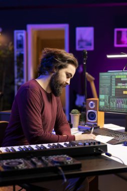 Ev stüdyosunda yeni bir şarkı yaratmak için kafiyeler ve sözler yazan genç besteci, harmonik notalar ve havalı müzik yapmak için replikler düşünüyor. Ses mühendisi teçhizatlı ses parçaları üretiyor.