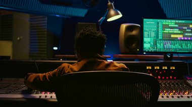 Afrikalı Amerikalı ses yapımcısı eski kayıtları karıştırma, işleme ve düzenleme konsoluna sarmalanmış kabloyu bağlıyor. Müzik yaratmak için düğmelere ve sürgülere basan teknisyenler. Kamera B.